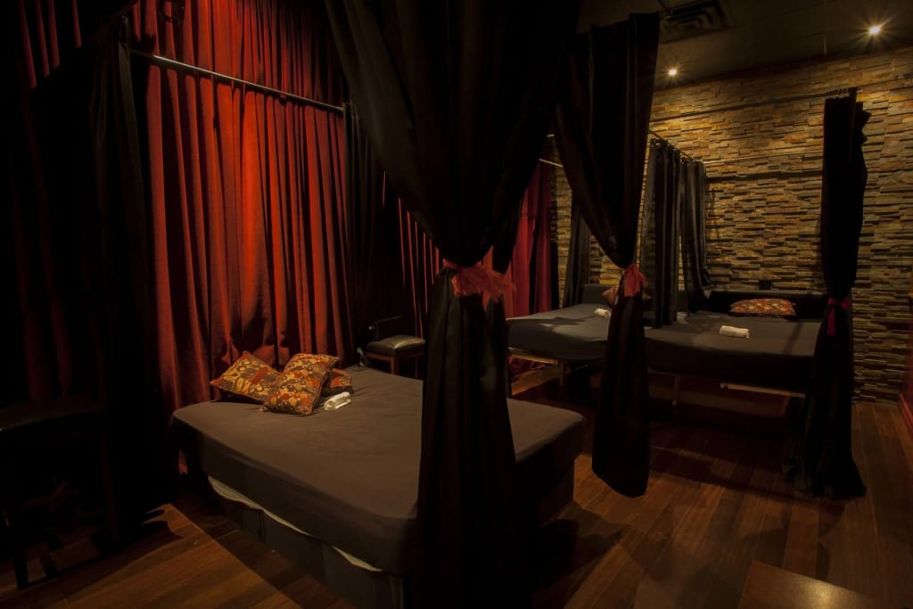 A private room with two massage-style beds, red curtains, patterned walls, and soft warm lighting, creating an intimate atmosphere for @wishpride.