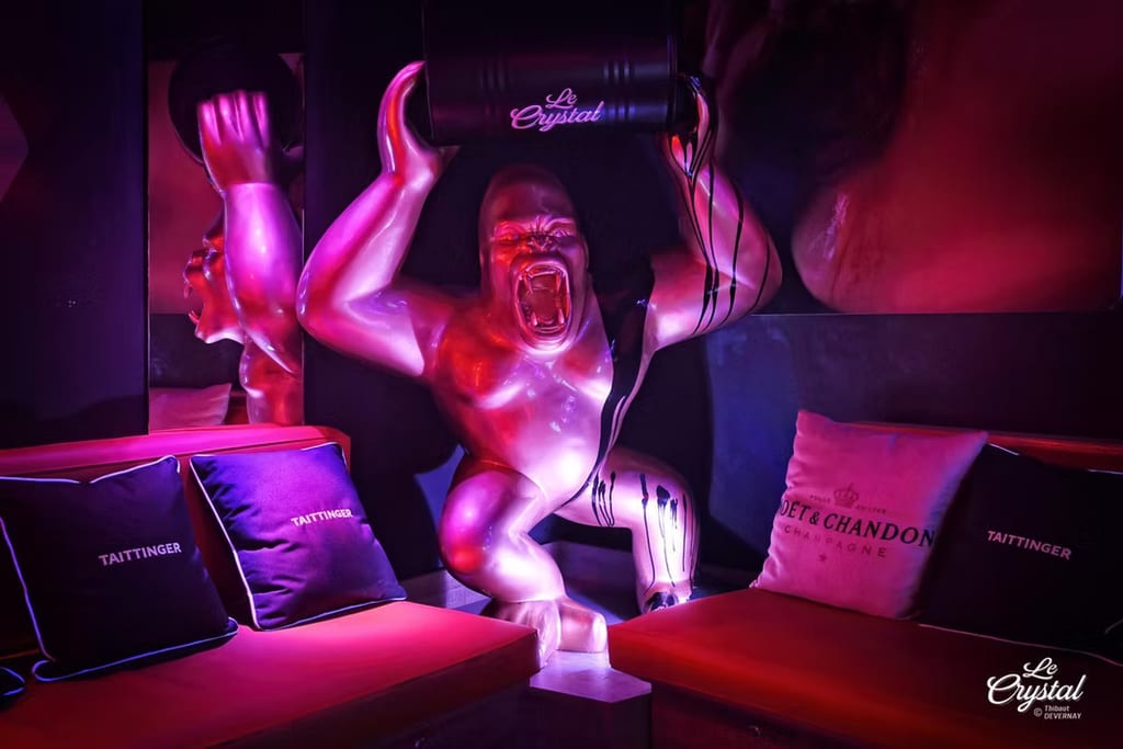 Lounge del Le Crystal con vivida illuminazione al neon magenta, sculture decorative illuminate e cuscini Taittinger brandizzati sulle sedute.
