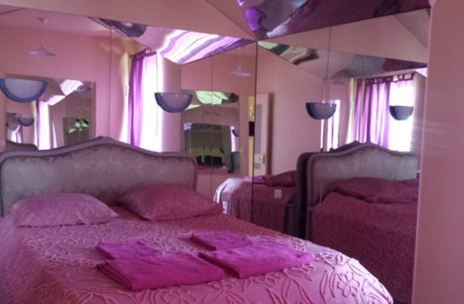 Stilvolle Suite mit großem Bett, violetten Vorhängen um hohe Fenster und Spiegelelementen für eine elegante Atmosphäre.
