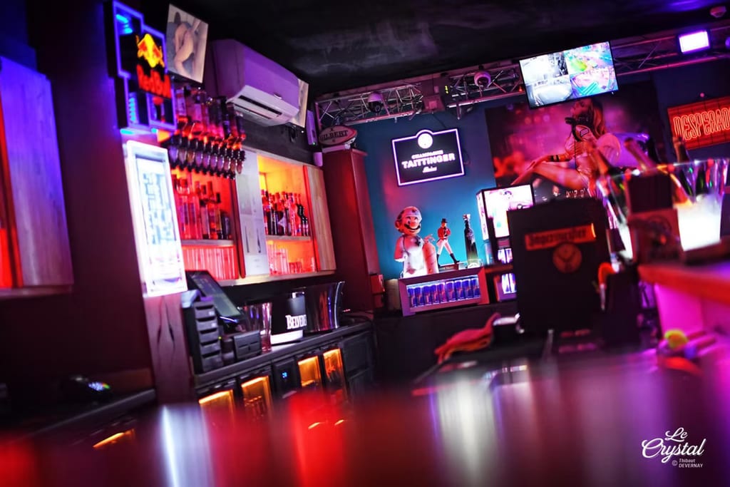 Espace bar éclairé au néon avec des étagères de bouteilles, des présentoirs à cocktails et des écrans au-dessus, à l’intérieur du Crystal au Cap d’Agde.